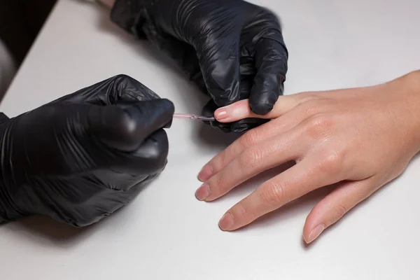 Manikyr svarta handskar göra manikyr på skönhetssalongen på en vit bakgrund. Nagellack färger naken. Vackra kvinnors händer — Stockfoto