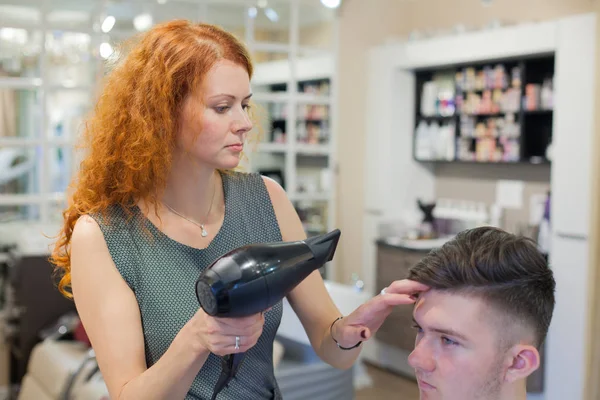 Male client getting haircut. Girl hairdresser dries my hair a young, attractive guy in a beauty salon — Stock Photo, Image