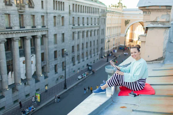 Çekici ve şık bir kız eski şehir Evin çatısı oturur ve e-kitap okur
