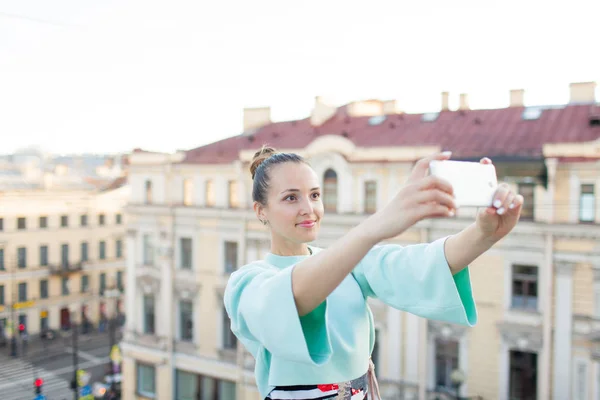 Nettes sexy Mädchen mit braunen Haaren steht auf dem Dach des Hauses in der Altstadt und macht ein Selfie auf dem Smartphone — Stockfoto