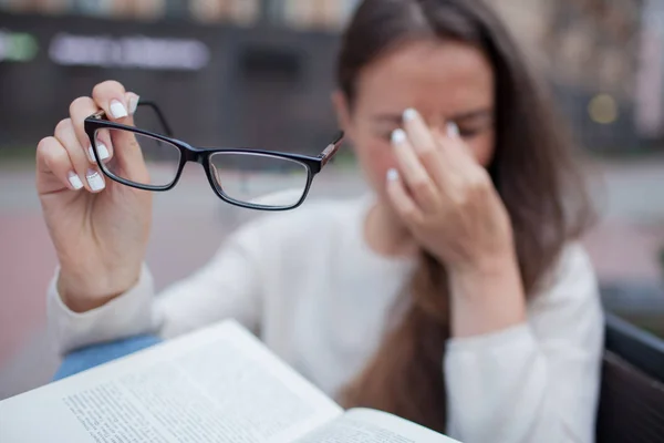 Closeup portrait of attractive female with eyeglasses in hand. Poor young girl has issues with vision. She rubs her nose and eyes out of fatigue. A student tired to study and read books — Stock Photo, Image