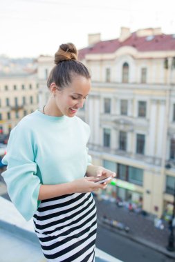 Güzel iş kadını manifatura telefon ve eski şehir Evin çatısı üzerinde dururken gülümseyen istemcilerle