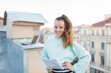 Bir belge tutarak ve eski şehir Evin çatısı üzerinde dururken gülümseyen çekici ve şık iş kadını
