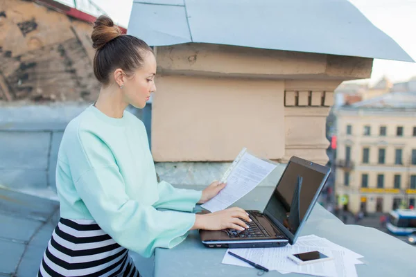 Empresária atraente e elegante prepara documentos para o telhado da casa na cidade velha de pé atrás de um laptop — Fotografia de Stock