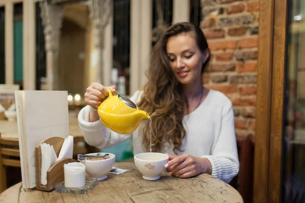 Rapariga sorridente no restaurante derrama chá verde do bule amarelo em uma xícara. Concentre-se em uma caneca de chá — Fotografia de Stock