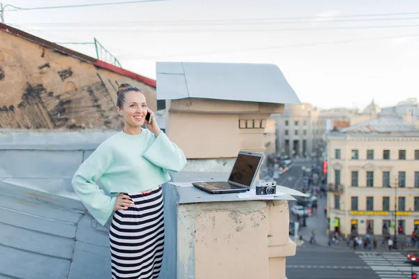 Nette Geschäftsfrau telefoniert auf dem Dach des Hauses in der Altstadt. Daneben liegen Laptop, Smartphone und Papierdokumente — Stockfoto