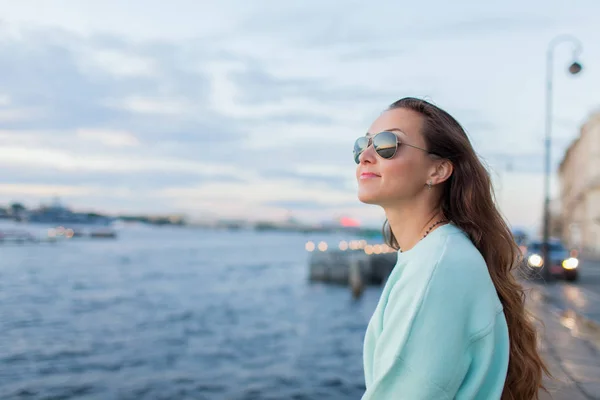 Menina jovem e bonita sentada no dique do rio. Ela olha para o pôr-do-sol e para os navios que passam. São Petersburgo, Rússia — Fotografia de Stock