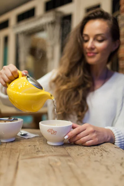 Restoranda genç kız gülümseyerek sarı çaydanlık bir fincan yeşil çay dökülen. Bir fincan çay üzerinde odaklanmak — Stok fotoğraf