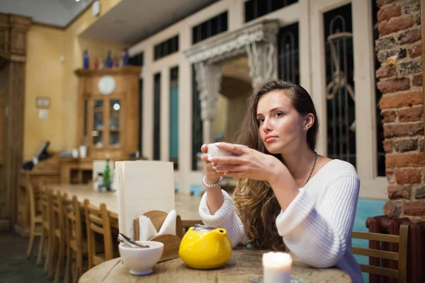 Vonzó és magányos lány ül egy kávézóban, teázás a sárga teáskannát. Néz ki az ablak, Gondolkozz és álom — Stock Fotó