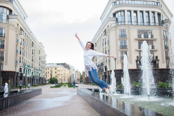 Junge sportliche Mädchen springen vor Freude am Brunnen in der Wohnanlage. Weibchen auf der Flucht mit erhobenen Händen — Stockfoto