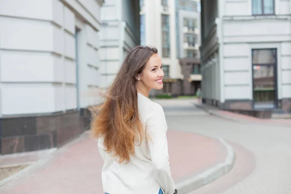 Uma menina jovem e atraente com cabelos castanhos longos em uma camisola leve montando uma scooter em um novo complexo residencial — Fotografia de Stock