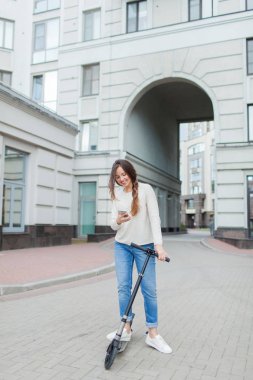 Uzun kahverengi saçlı güzel, genç ve beyaz dişli kız arkadaşıma telefonda yazmak için sürme sırasında durdu. O beyaz bir kazak ve mavi kot pantolon giymiş. Kentsel arka plan