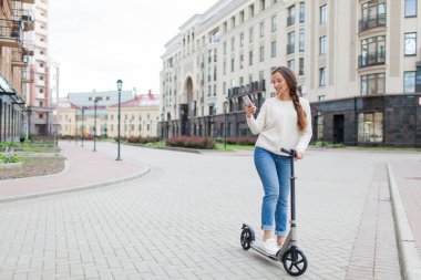 Uzun kahverengi saçlı güzel, genç ve beyaz dişli kız arkadaşıma telefonda yazmak için sürme sırasında durdu. O beyaz bir kazak ve mavi kot pantolon giymiş. Kentsel arka plan