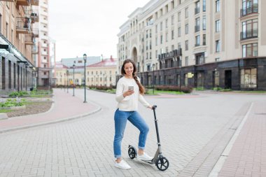 Uzun kahverengi saçlı güzel, genç ve beyaz dişli kız arkadaşıma telefonda yazmak için sürme sırasında durdu. O beyaz bir kazak ve mavi kot pantolon giymiş. Kentsel arka plan