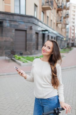 Uzun kahverengi saçlı güzel genç kız arkadaşıma telefonda yazmak için sürme sırasında durdu. O beyaz bir kazak ve mavi kot pantolon giymiş. Kentsel arka plan