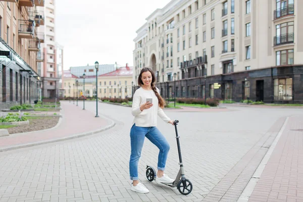 Uzun kahverengi saçlı güzel, genç ve beyaz dişli kız arkadaşıma telefonda yazmak için sürme sırasında durdu. O beyaz bir kazak ve mavi kot pantolon giymiş. Kentsel arka plan