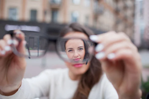 Closeup portrait of young women with glasses. She has eyesight problems and is squinting his eyes a little bit. Beautiful girl is holding eyeglasses right in front of camera with two hand — Stock Photo, Image