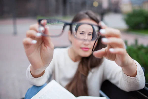 Närbild porträtt av unga kvinnor med glasögon. Hon har problem med syn och vindögd ögonen lite. Vacker flicka håller glasögon precis framför kameran med två hand — Stockfoto