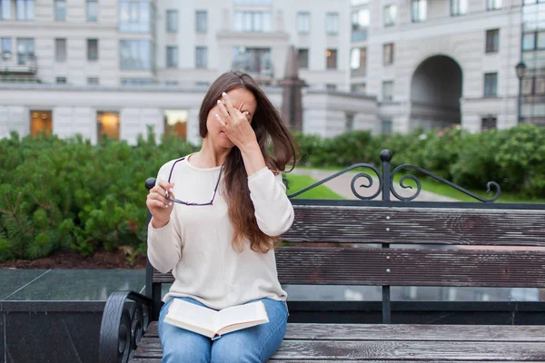 Primer plano retrato de atractiva hembra con gafas en la mano. La pobre jovencita tiene problemas con la visión. Se frota la nariz y los ojos por fatiga. Un estudiante cansado de estudiar y leer libros —  Fotos de Stock