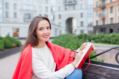 Çekici kız çıplak ayaklı bir bankta oturan yeni yerleşim bölgesinde kırmızı bir battaniye ile örtülü ve düşüncelerini içine kırmızı bir defter yazıyor. Kentsel arka plan