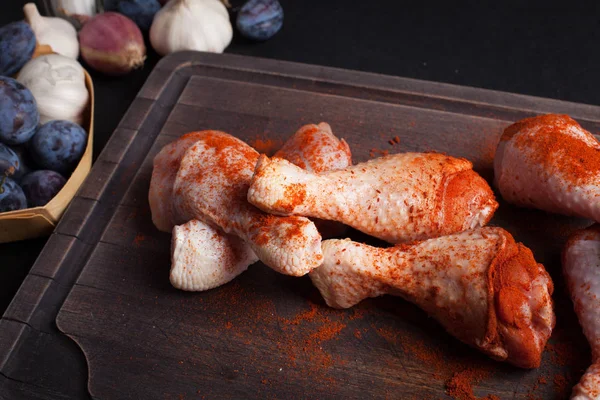 Karanlık bir arka plan üzerine sarımsak, kırmızı biber, tuz ve biber karışımı ile çiğ tavuk uyluk closeup. Üstten Görünüm. Kesme çevresinde ayrıca yönetim kurulu arpacık ve Erik