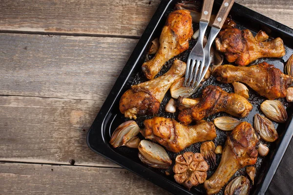 Oven baked chicken legs with onions, garlic and peppers on a dark wooden background closeup. Top view with copy space. Wooden rustic table — Stock Photo, Image