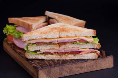 Jambon, peynir, domates ve karanlık bir arka plan üzerinde kızarmış ekmek üzerinde salata ile yakın çekim büyük sandviç