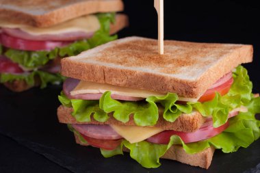 Jambon, peynir, domates ve karanlık bir arka plan üzerinde kızarmış ekmek üzerinde salata ile yakın çekim büyük sandviç