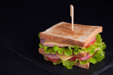 Jambon, peynir, domates ve salata karanlık bir arka plan üzerinde kızarmış ekmek üzerinde yakın çekim büyük sandviçle. Kopya alanı