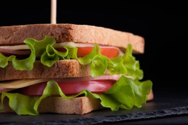 Jambon, peynir, domates ve karanlık bir arka plan üzerinde kızarmış ekmek üzerinde salata ile yakın çekim büyük sandviç