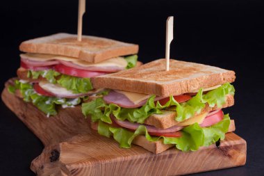 Jambon, peynir, domates ve karanlık bir arka plan üzerinde kızarmış ekmek üzerinde salata ile yakın çekim büyük sandviç