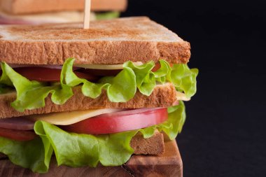 Jambon, peynir, domates ve karanlık bir arka plan üzerinde kızarmış ekmek üzerinde salata ile yakın çekim büyük sandviç