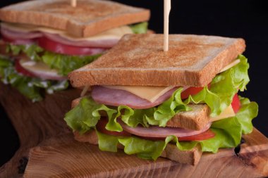 Jambon, peynir, domates ve karanlık bir arka plan üzerinde kızarmış ekmek üzerinde salata ile yakın çekim büyük sandviç