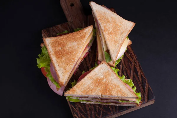 Крупним планом великий бутерброд з шинкою, сиром, помідорами та салатом на підсмаженому хлібі на темному тлі. Вид зверху — стокове фото