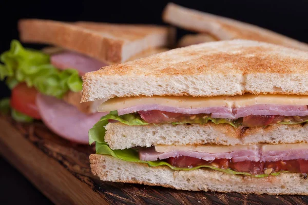 Zbliżenie, duże sandwich z szynką, serem, pomidorami i sałatka na tosty na ciemnym tle — Zdjęcie stockowe