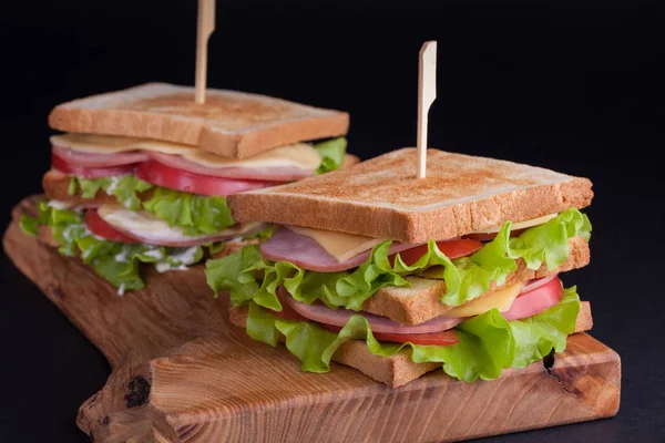 Jambon, peynir, domates ve karanlık bir arka plan üzerinde kızarmış ekmek üzerinde salata ile yakın çekim büyük sandviç