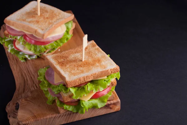 Jambon, peynir, domates ve salata karanlık bir arka plan üzerinde kızarmış ekmek üzerinde yakın çekim büyük sandviçle. Kopya alanı
