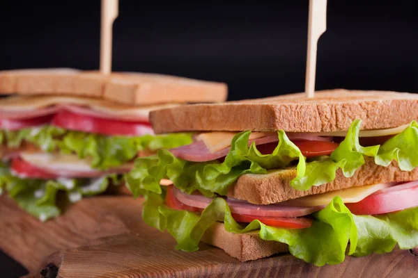Jambon, peynir, domates ve karanlık bir arka plan üzerinde kızarmış ekmek üzerinde salata ile yakın çekim büyük sandviç