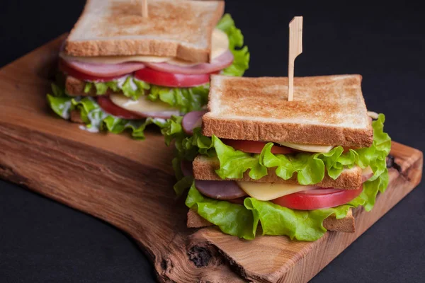 Primo piano grande panino con prosciutto, formaggio, pomodori e insalata su pane tostato su sfondo scuro — Foto Stock