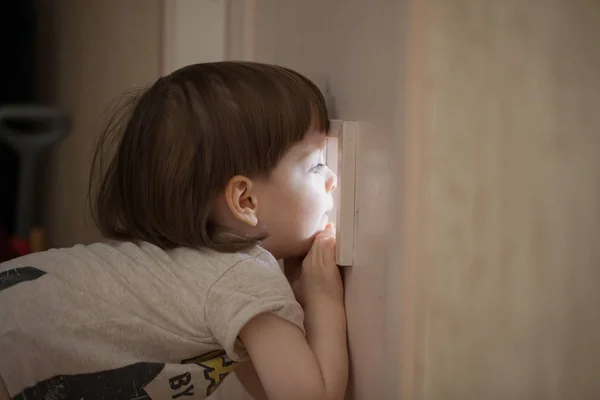 The little boy looks in the window of the door. A child spying on his parents from behind the closed bedroom door — Stock Photo, Image