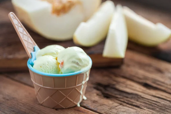 Vanilleeis mit Melonengeschmack in einer Schüssel auf einem alten Holztisch. auf dem Hintergrund einer aufgeschnittenen frischen Melone — Stockfoto