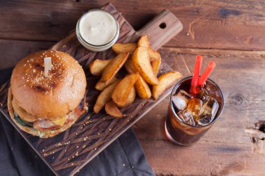 Aperatifler beyaz Sarımsak soslu patates şeklinde ve soğuk kola bir bardak ile lezzetli bir Burger. soğan halkaları, pastırma ve koyu ahşap arka plan üzerinde peynir ile sulu Burger.