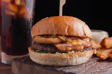 Aperatifler beyaz Sarımsak soslu patates şeklinde ve soğuk kola bir bardak ile lezzetli bir Burger. soğan halkaları, pastırma ve koyu ahşap arka plan üzerinde peynir ile sulu Burger