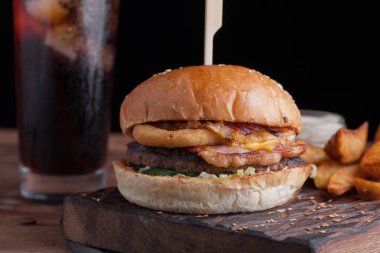 Aperatifler beyaz Sarımsak soslu patates şeklinde ve soğuk kola bir bardak ile lezzetli bir Burger. soğan halkaları, pastırma ve koyu ahşap arka plan üzerinde peynir ile sulu Burger.