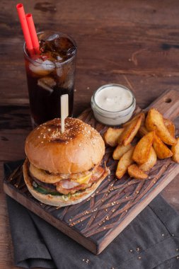 Aperatifler beyaz Sarımsak soslu patates şeklinde ve soğuk kola bir bardak ile lezzetli bir Burger. soğan halkaları, pastırma ve koyu ahşap arka plan üzerinde peynir ile sulu Burger.