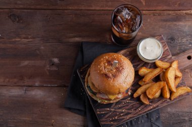Aperatifler beyaz Sarımsak soslu patates şeklinde ve soğuk kola bir bardak ile lezzetli bir Burger. soğan halkaları, pastırma ve koyu ahşap arka plan üzerinde peynir ile sulu Burger.