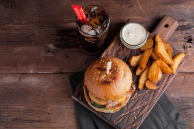 Aperatifler beyaz Sarımsak soslu patates şeklinde ve soğuk kola bir bardak ile lezzetli bir Burger. soğan halkaları, pastırma ve koyu ahşap arka plan üzerinde peynir ile sulu Burger