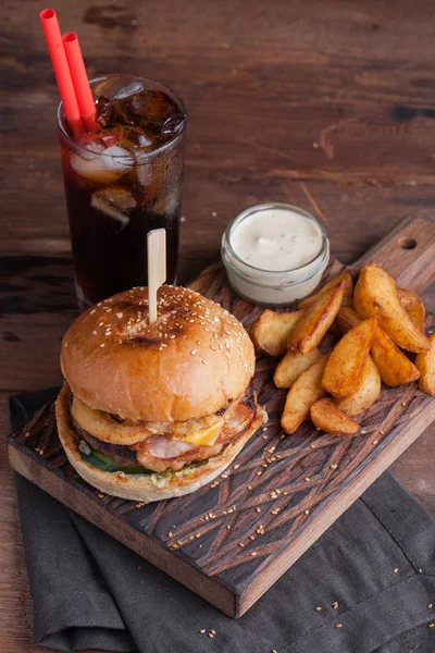 Aperatifler beyaz Sarımsak soslu patates şeklinde ve soğuk kola bir bardak ile lezzetli bir Burger. soğan halkaları, pastırma ve koyu ahşap arka plan üzerinde peynir ile sulu Burger.
