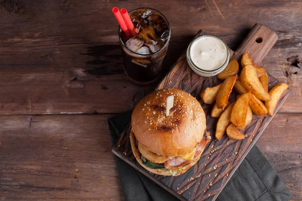 Aperatifler beyaz Sarımsak soslu patates şeklinde ve soğuk kola bir bardak ile lezzetli bir Burger. soğan halkaları, pastırma ve koyu ahşap arka plan üzerinde peynir ile sulu Burger