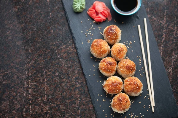 Japonská kuchyně. Pečené sushi s krabím masem a sýrem na kamenné desce na pozadí černé žuly. Pohled shora s kopií prostor — Stock fotografie